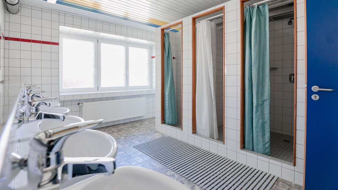 Salle de bain carrelée blanche dans la maison d’été avec plusieurs lavabos et douches