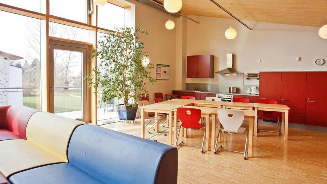 Espace commun supérieur dans le Wiesenhaus avec balcon: avec kitchenette rouge, groupe de tables à manger et coin salon au premier plan
