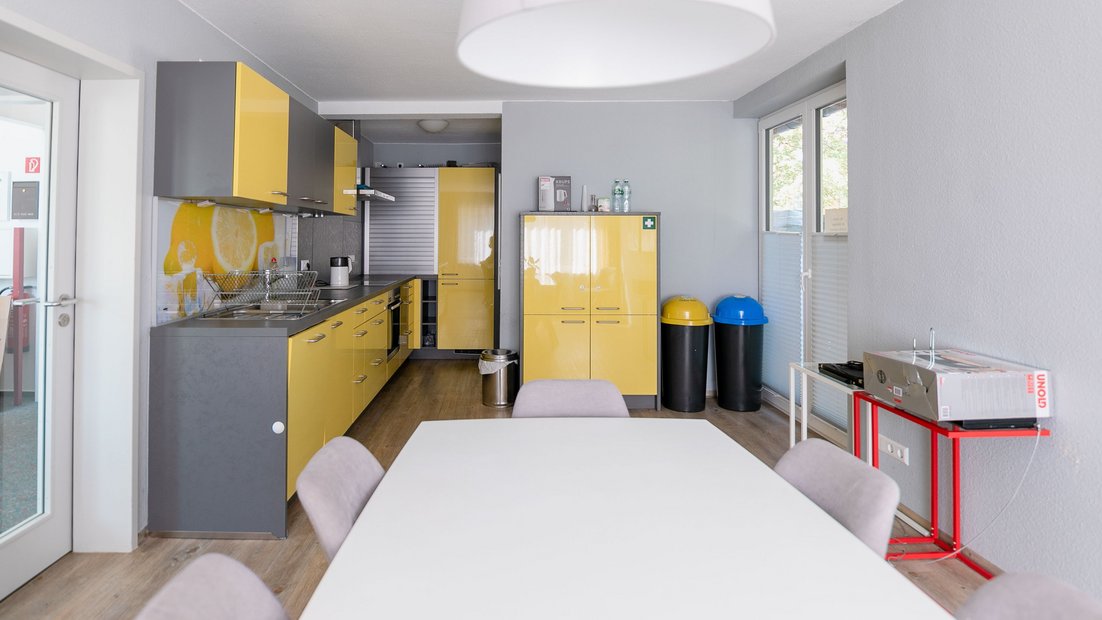 Kitchenette moderne en gris-jaune avec groupe de tables à manger au premier plan