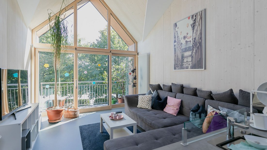 Espace commun confortable à l’étage avec grand coin canapé gris et vue à travers une grande fenêtre de balcon