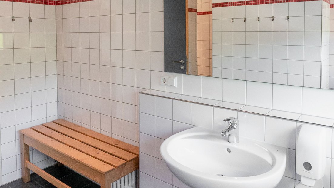 Salle de bain carrelée blanche avec lavabo et miroir dans l’abri de jardin
