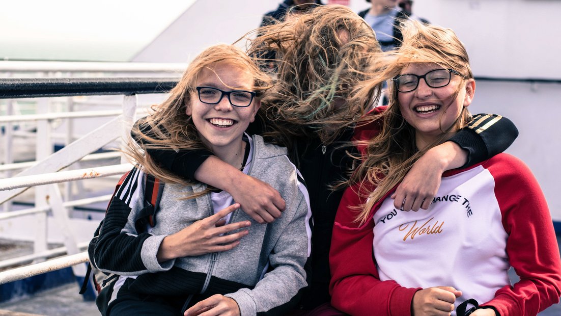 Trois filles sur le pont d’un navire rient devant la caméra.